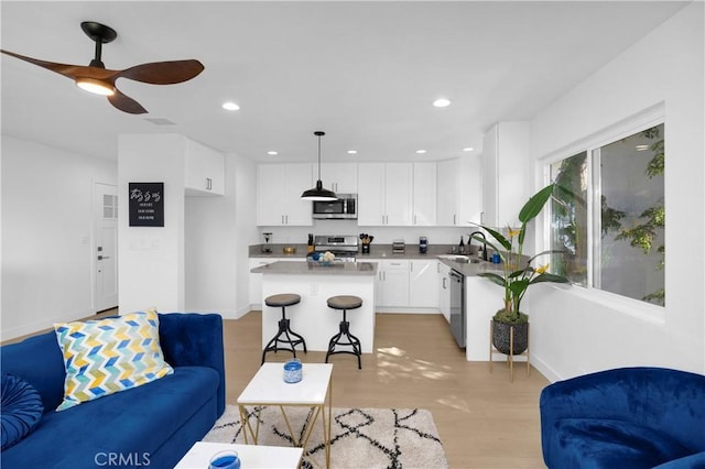 living room with light wood-type flooring, ceiling fan, and sink