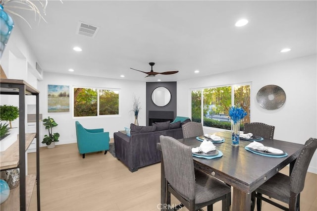 dining space with a fireplace, ceiling fan, and light hardwood / wood-style flooring