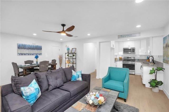 living room with ceiling fan, sink, and light wood-type flooring