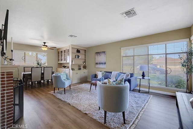 living room with ceiling fan, a brick fireplace, hardwood / wood-style flooring, and plenty of natural light