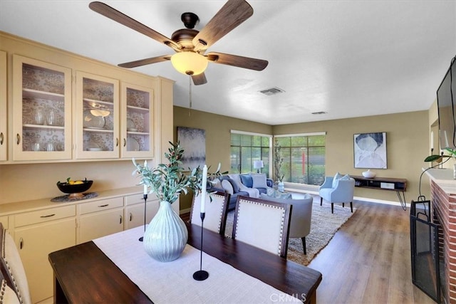 dining room featuring ceiling fan, a brick fireplace, and light hardwood / wood-style floors