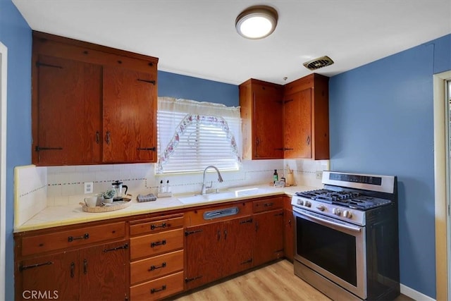 kitchen with stainless steel gas range oven, sink, light hardwood / wood-style floors, and tasteful backsplash