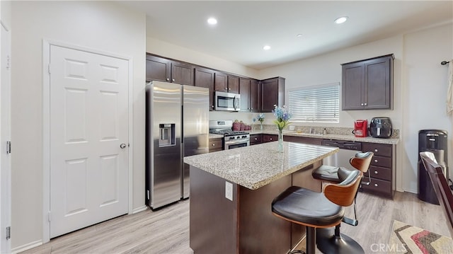 kitchen featuring light hardwood / wood-style floors, a kitchen island, a breakfast bar area, stainless steel appliances, and dark brown cabinets