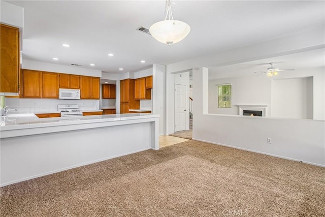 kitchen featuring white appliances, sink, hanging light fixtures, light colored carpet, and kitchen peninsula