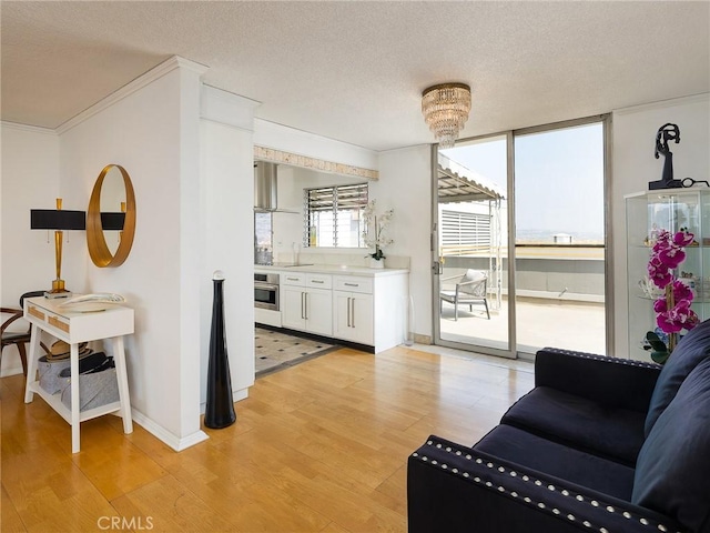 living room featuring a chandelier, light hardwood / wood-style floors, a textured ceiling, and ornamental molding