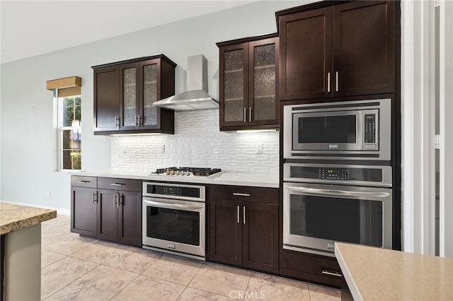 kitchen featuring dark brown cabinetry, stainless steel appliances, wall chimney exhaust hood, and light tile patterned floors