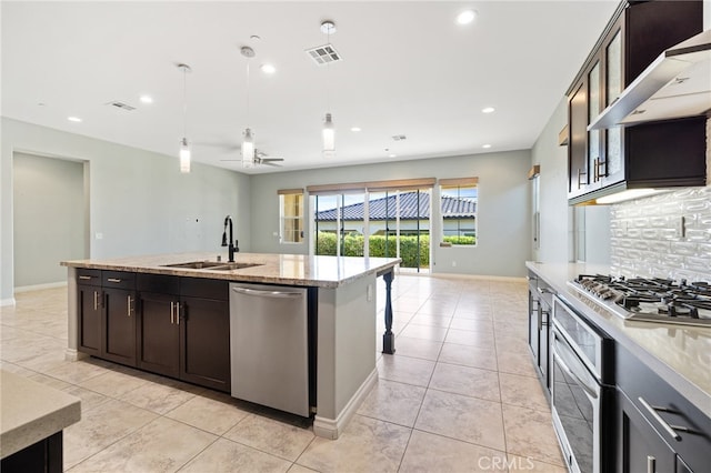 kitchen featuring sink, an island with sink, stainless steel appliances, backsplash, and ceiling fan