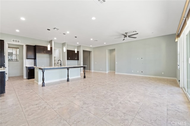 kitchen with hanging light fixtures, ceiling fan, an island with sink, and plenty of natural light