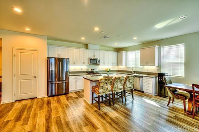 kitchen with appliances with stainless steel finishes, white cabinets, a breakfast bar area, light wood-type flooring, and a center island