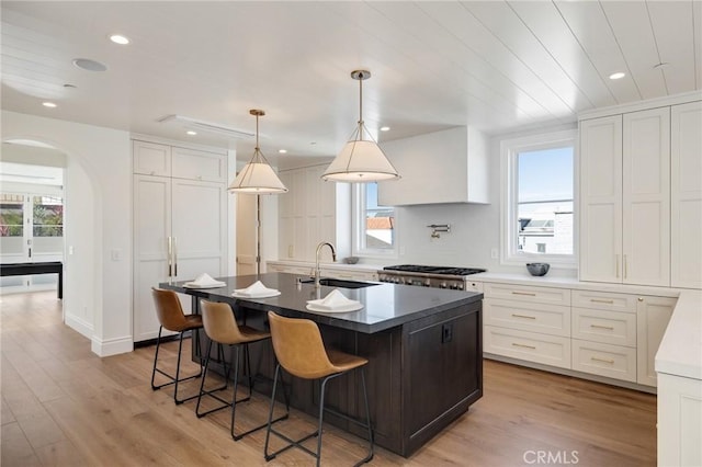 kitchen featuring white cabinetry, sink, hanging light fixtures, and an island with sink