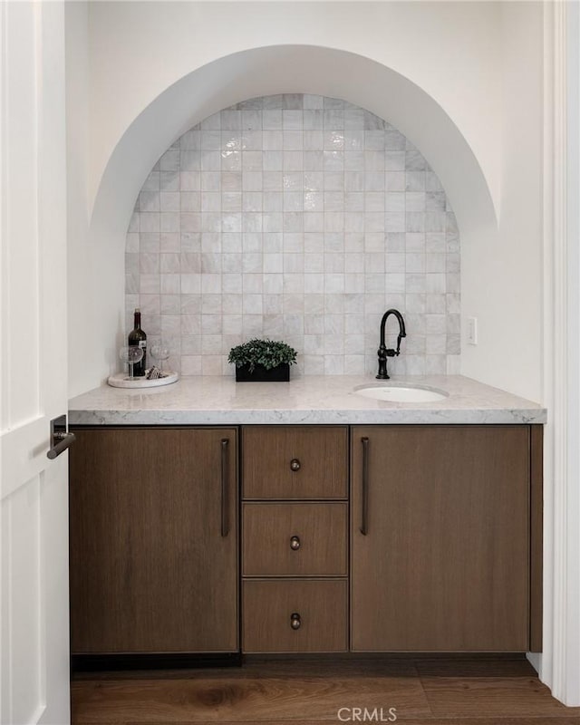 bar featuring light stone counters, sink, dark wood-type flooring, and tasteful backsplash