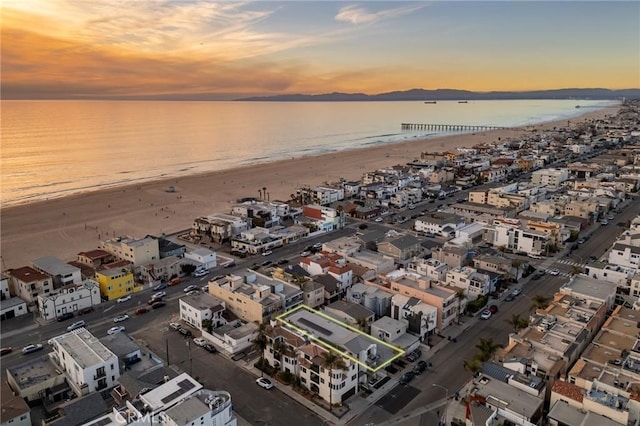 aerial view at dusk with a water view and a view of the beach