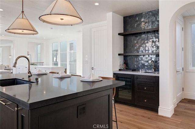 kitchen with hanging light fixtures, sink, a center island with sink, and light hardwood / wood-style flooring