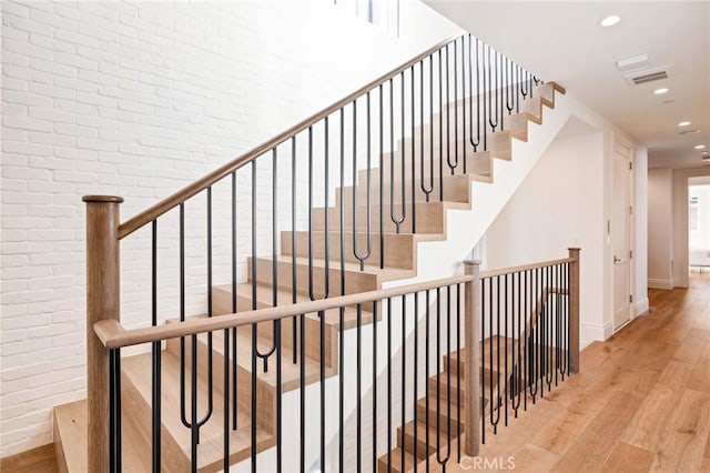 stairs featuring brick wall and hardwood / wood-style floors