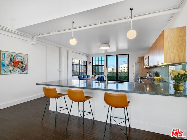 kitchen featuring kitchen peninsula, appliances with stainless steel finishes, dark wood-type flooring, sink, and decorative light fixtures