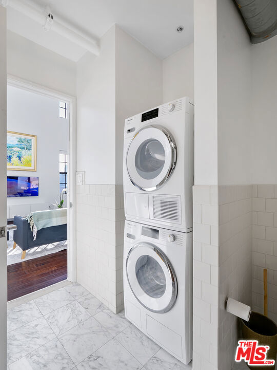 laundry area with tile walls and stacked washer and clothes dryer