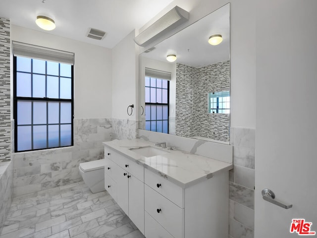 bathroom with vanity, a healthy amount of sunlight, and tile walls