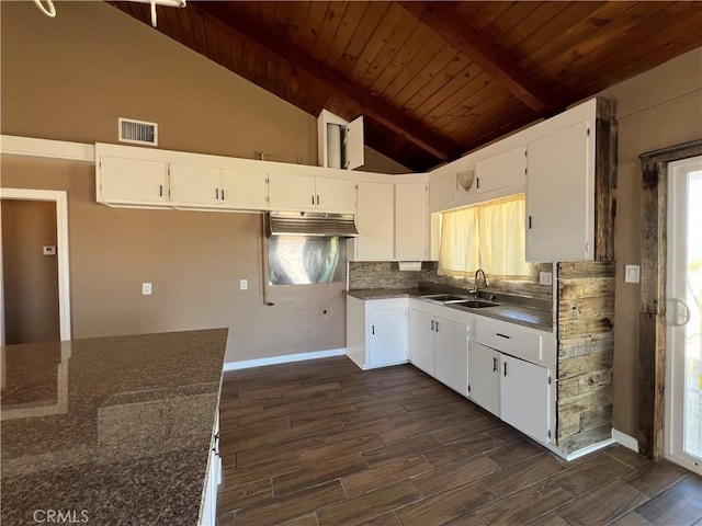 kitchen with beam ceiling, white cabinetry, dark stone countertops, and sink