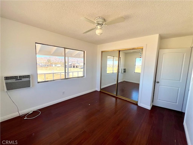 unfurnished bedroom featuring a wall mounted air conditioner, a textured ceiling, ceiling fan, dark hardwood / wood-style floors, and a closet