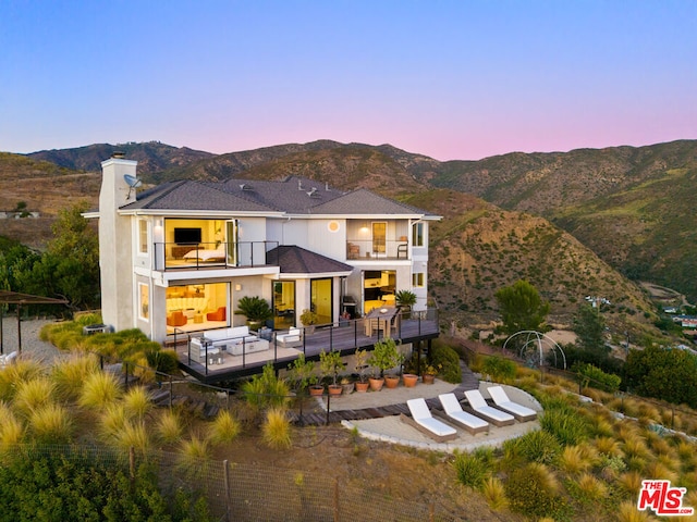 back house at dusk with a balcony, outdoor lounge area, and a mountain view