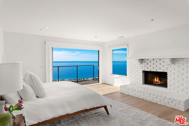 bedroom with light wood-type flooring, a fireplace, and a water view