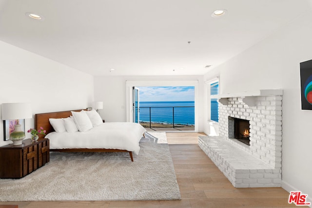 bedroom with access to outside, a fireplace, light hardwood / wood-style floors, and a water view