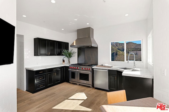 kitchen featuring sink, light hardwood / wood-style flooring, wall chimney range hood, stainless steel appliances, and decorative backsplash