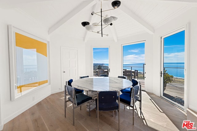 dining room featuring a chandelier, hardwood / wood-style floors, a water view, and lofted ceiling with beams