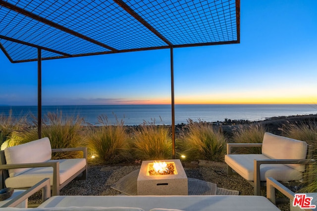 patio terrace at dusk featuring a fire pit, a pergola, and a water view