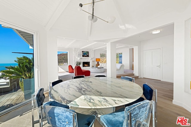 dining room with beamed ceiling, a water view, a large fireplace, and light hardwood / wood-style flooring