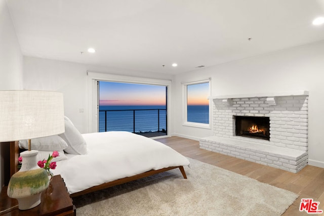 bedroom featuring a brick fireplace, light hardwood / wood-style floors, and a water view