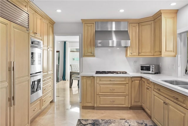 kitchen featuring paneled fridge, a toaster, gas stovetop, light countertops, and wall chimney range hood