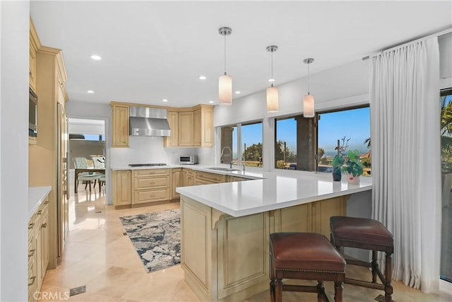 kitchen featuring gas stovetop, wall chimney exhaust hood, light brown cabinets, and light countertops