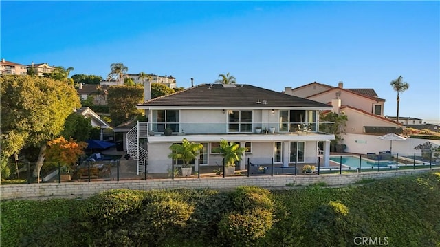 back of house with stucco siding, a patio area, a balcony, and a fenced in pool