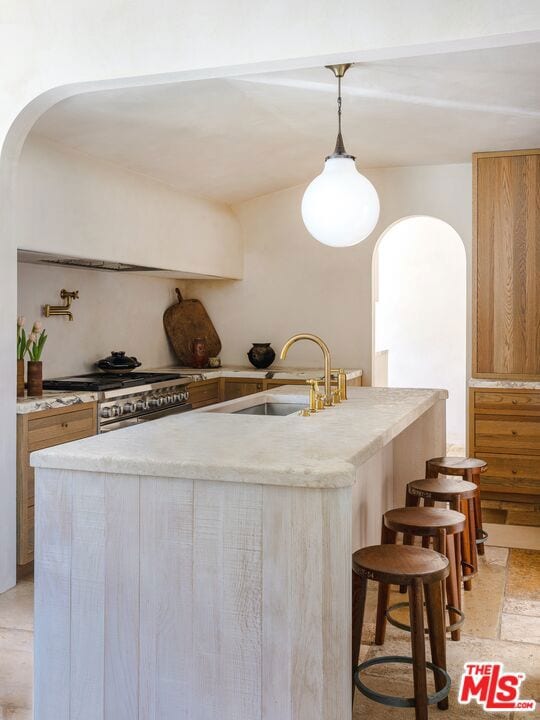 kitchen featuring stainless steel range, a kitchen island with sink, decorative light fixtures, and sink