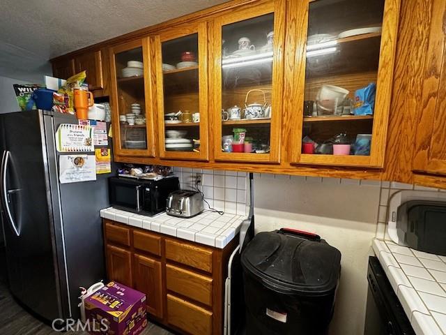 kitchen with brown cabinets, freestanding refrigerator, and tile countertops