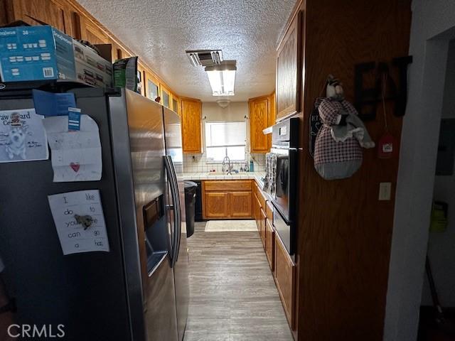 kitchen with stainless steel fridge with ice dispenser, light countertops, visible vents, black oven, and a textured ceiling