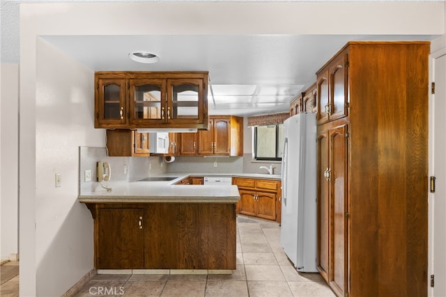 kitchen featuring white appliances, kitchen peninsula, light tile patterned floors, and sink