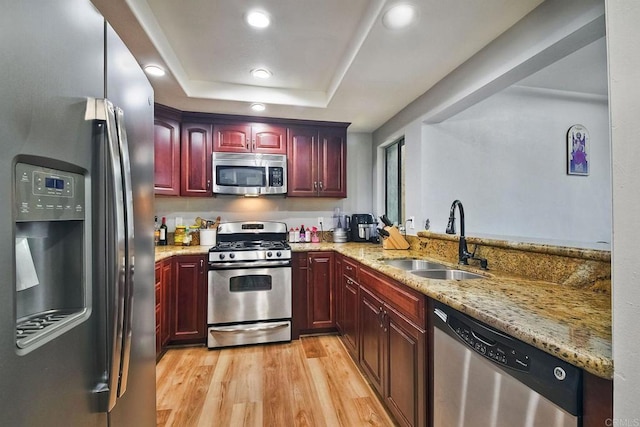 kitchen with a raised ceiling, sink, light wood-type flooring, light stone counters, and stainless steel appliances