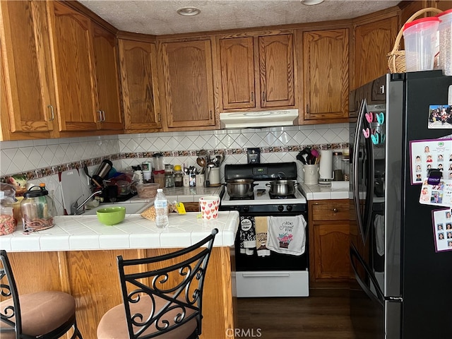 kitchen featuring stainless steel refrigerator, kitchen peninsula, dark hardwood / wood-style flooring, tile countertops, and white gas stove