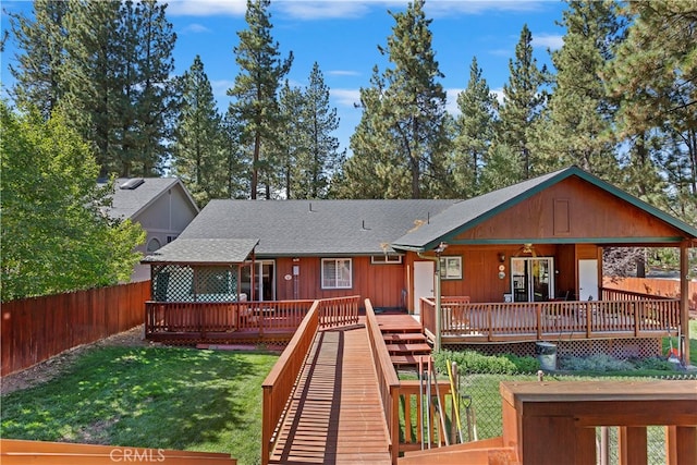 back of property featuring a shingled roof, a wooden deck, a lawn, and a fenced backyard