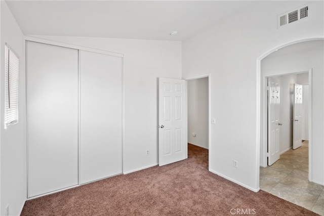 unfurnished bedroom with lofted ceiling, light carpet, and a closet