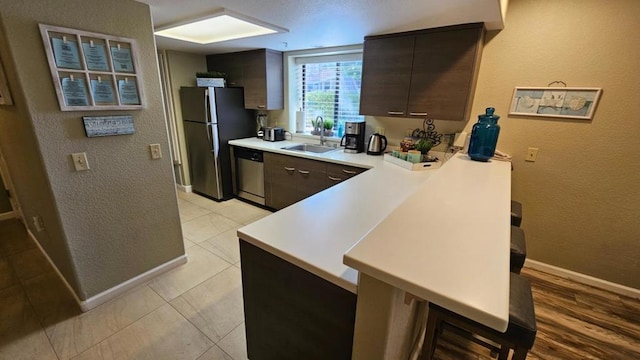 kitchen featuring sink, a kitchen bar, appliances with stainless steel finishes, light tile patterned floors, and dark brown cabinetry