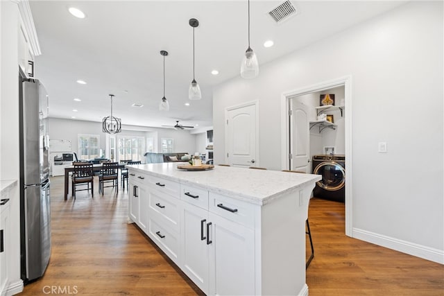 kitchen featuring wood-type flooring, a center island, white cabinetry, decorative light fixtures, and light stone countertops