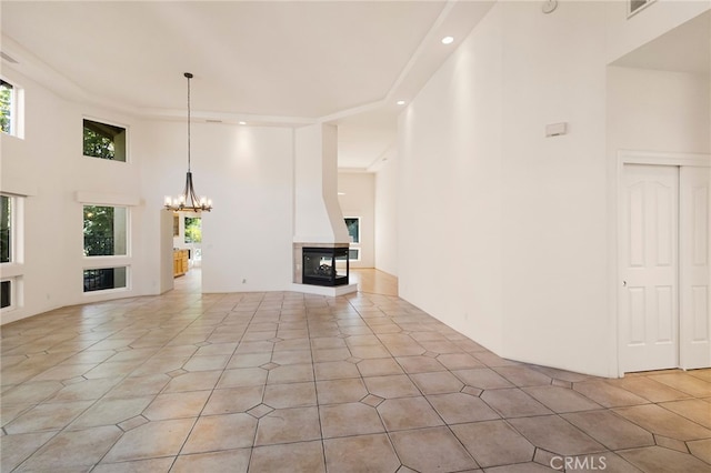 unfurnished living room featuring a high ceiling, a multi sided fireplace, light tile patterned flooring, and a notable chandelier