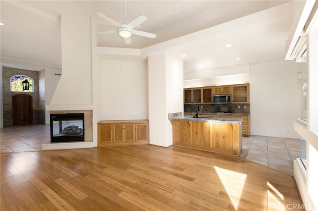 kitchen with a multi sided fireplace, sink, decorative backsplash, light hardwood / wood-style floors, and kitchen peninsula