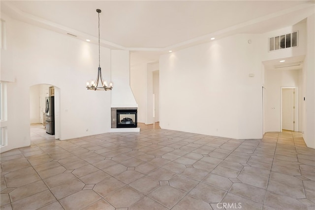 unfurnished living room with a multi sided fireplace, a towering ceiling, and an inviting chandelier