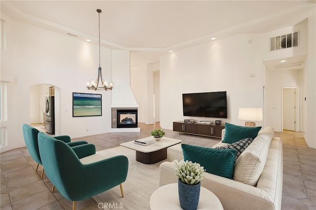 living room with an inviting chandelier, a multi sided fireplace, light tile patterned floors, and a high ceiling