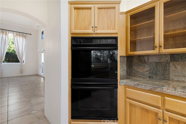 kitchen featuring light brown cabinetry, backsplash, black double oven, light tile patterned floors, and light stone counters