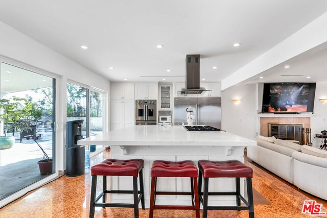 kitchen with a breakfast bar, white cabinets, island range hood, and stainless steel appliances